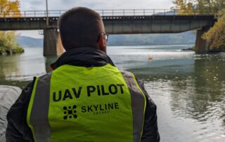 Person wearing a vest labeled UAV Pilot looking toward a bridge over a river